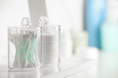 Containers with cotton swabs and pads on white shelf in bathroom, closeup. Space for text