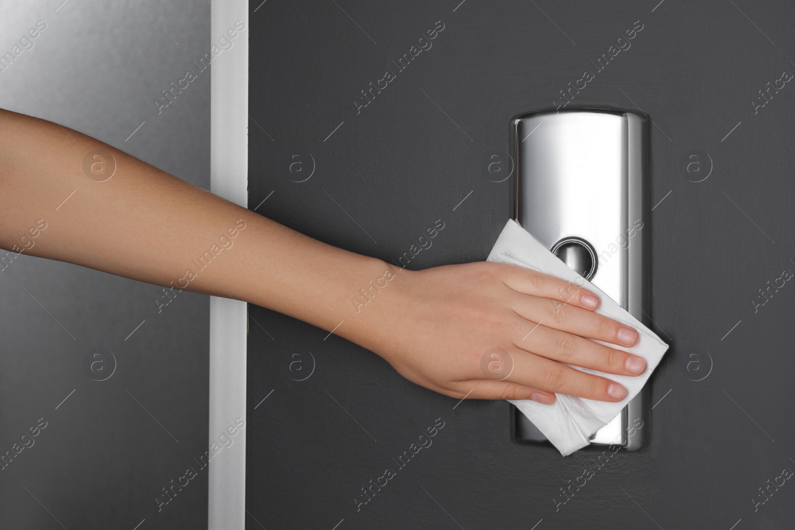 Photo of Woman cleaning elevator button with paper towel indoors, closeup