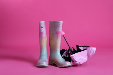 Closed umbrella and rubber boots on pink background
