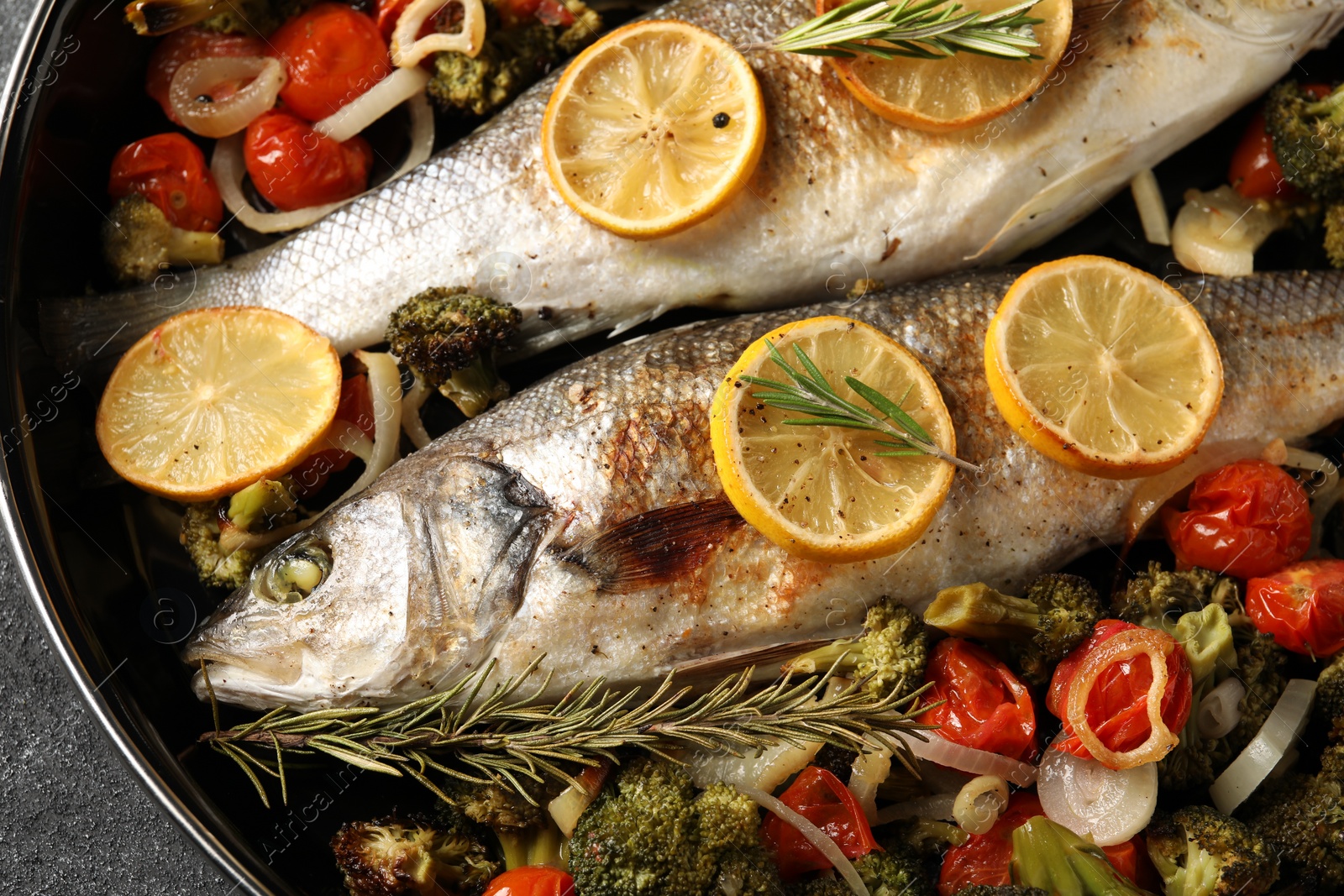 Photo of Baked fish with vegetables, rosemary and lemon on black textured table, top view