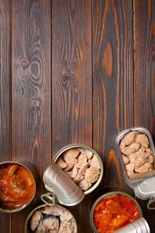 Photo of Tin cans with fish on wooden table, flat lay. Space for text