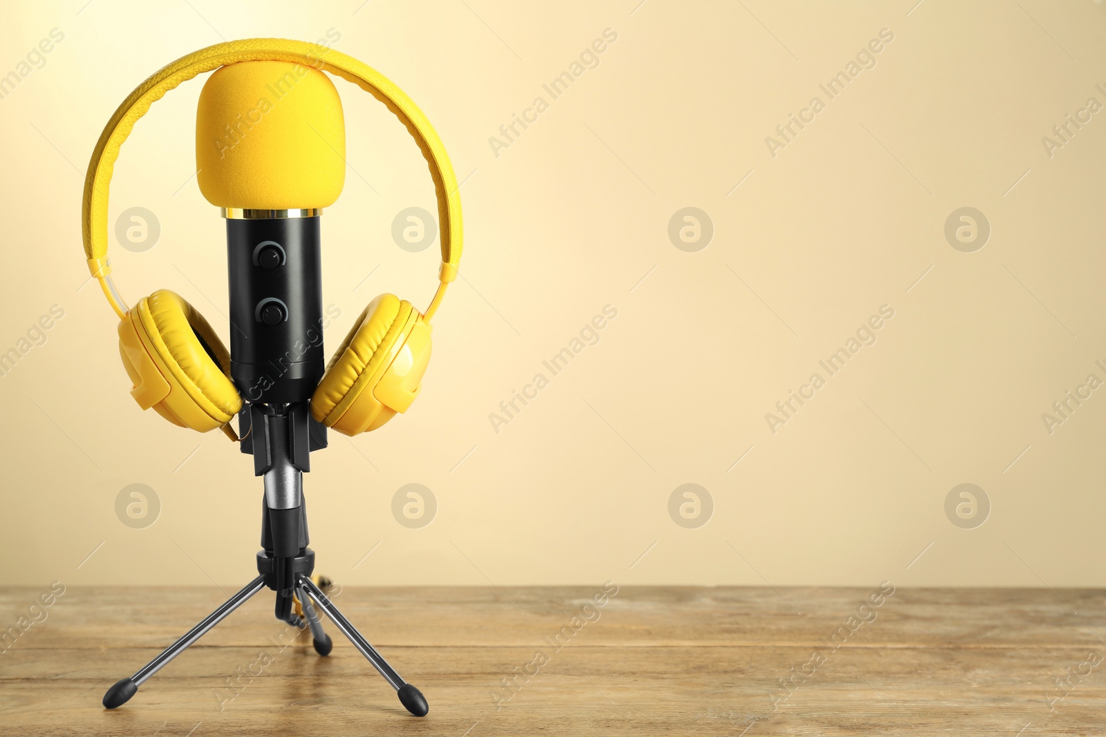 Photo of Microphone and modern headphones on wooden table against beige background, space for text