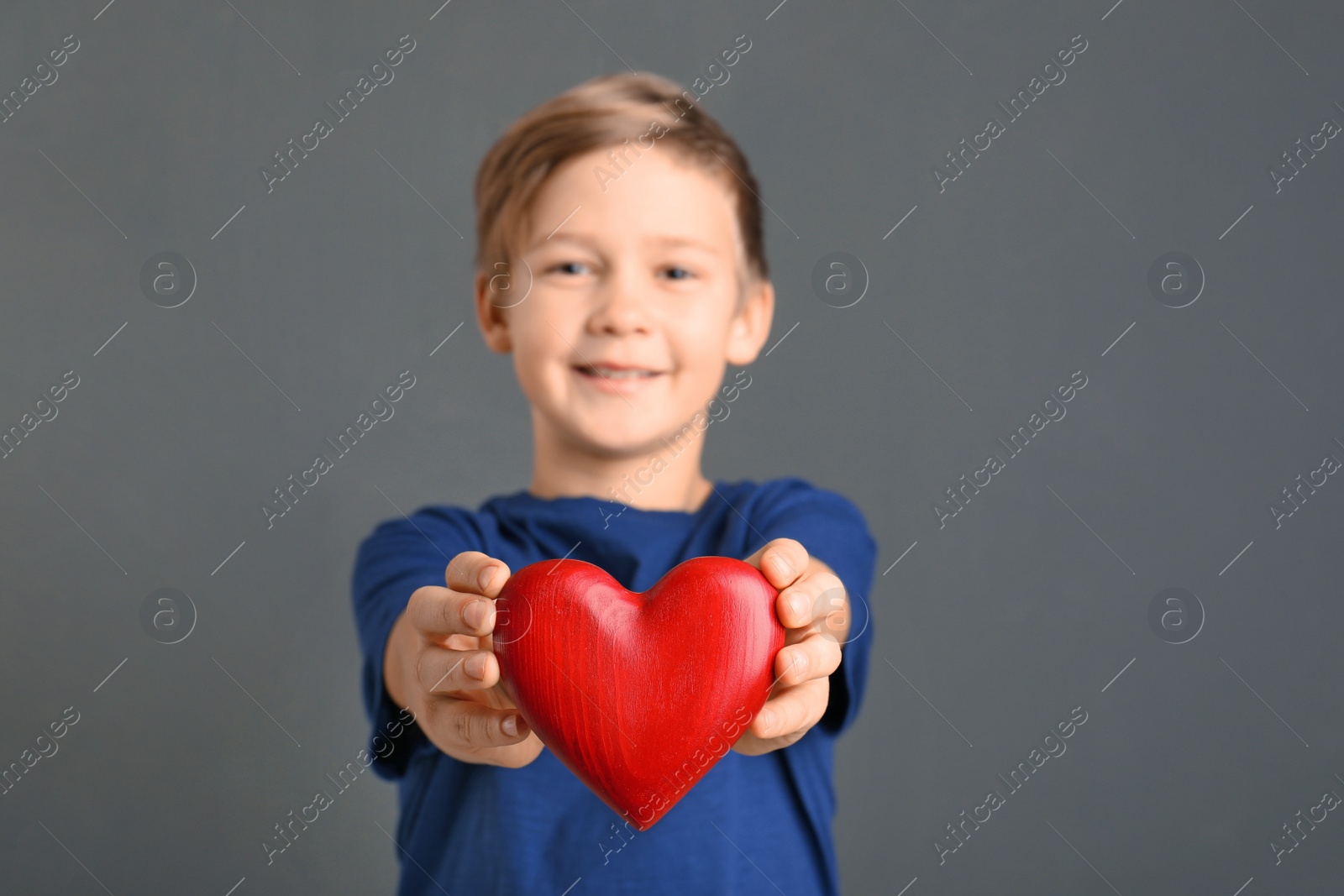 Photo of Cute boy holding wooden heart on grey background