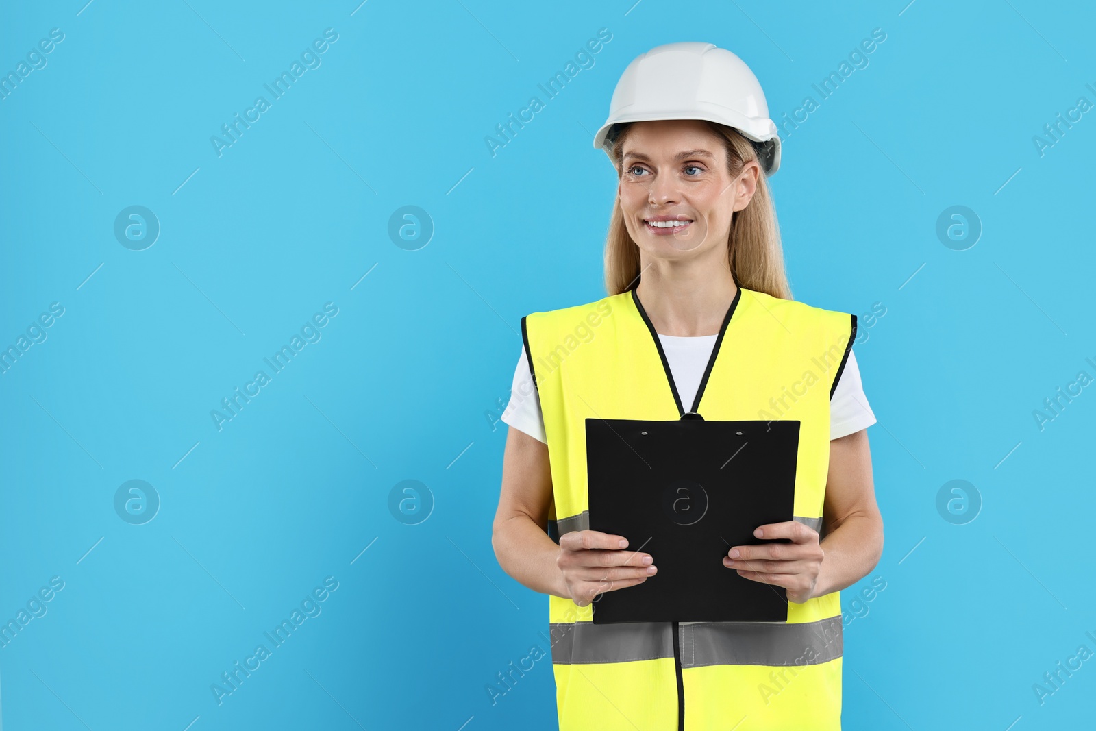 Photo of Engineer in hard hat holding clipboard on light blue background, space for text