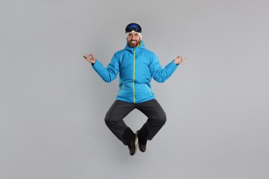 Photo of Winter sports. Happy man in ski suit and goggles jumping on gray background