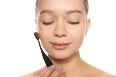 Young woman applying foundation on her face against white background