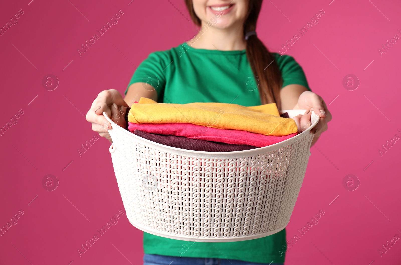 Photo of Young woman holding basket with laundry on color background, closeup
