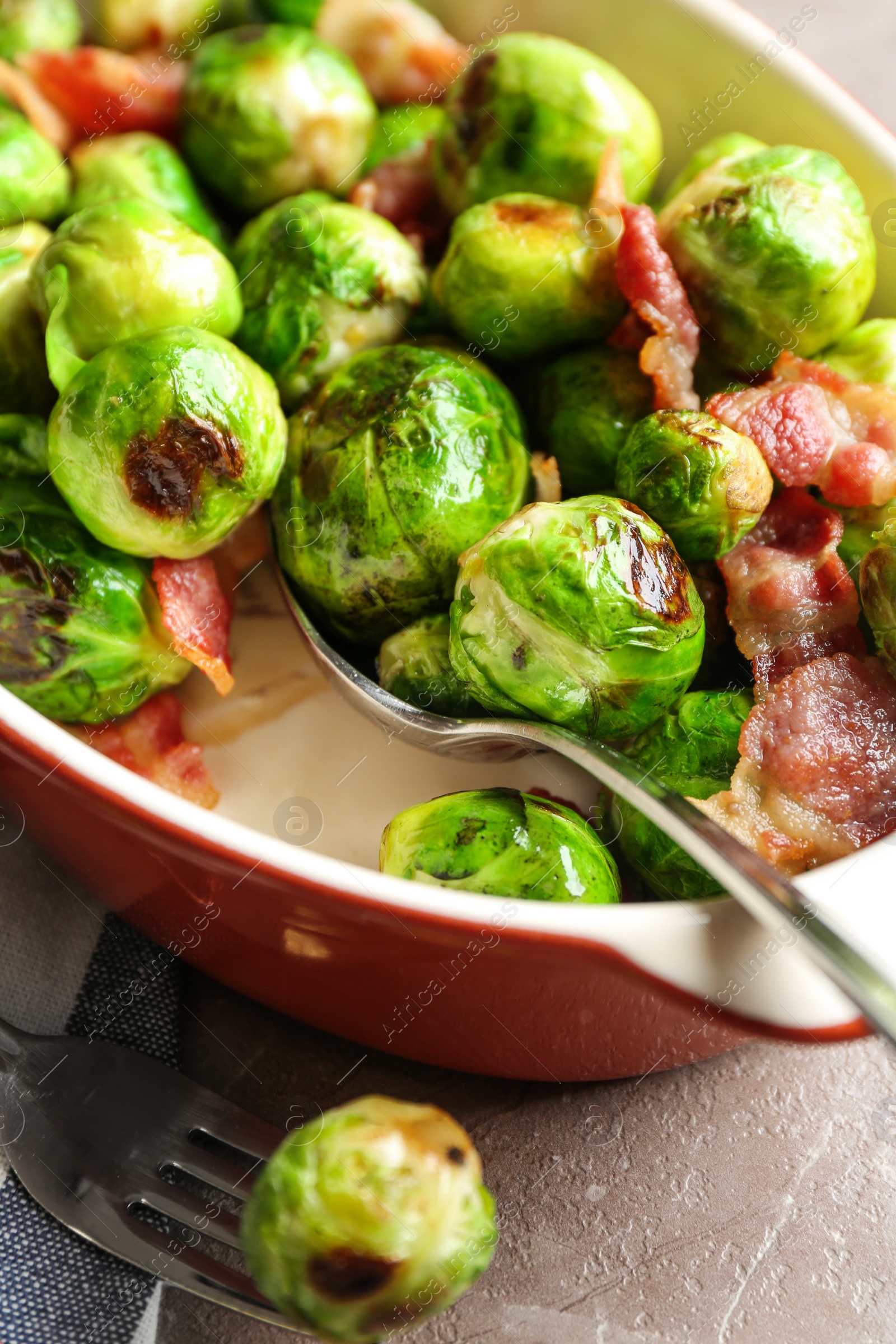 Photo of Delicious Brussels sprouts with bacon in baking dish on marble table, closeup