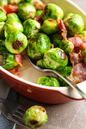 Photo of Delicious Brussels sprouts with bacon in baking dish on marble table, closeup