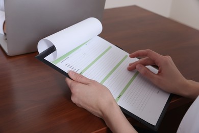 Woman holding medical card at wooden table in conference room, closeup