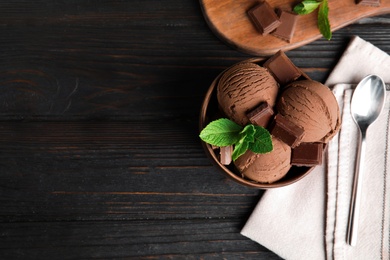 Photo of Flat lay composition with bowl of chocolate ice cream and mint on wooden table, space for text