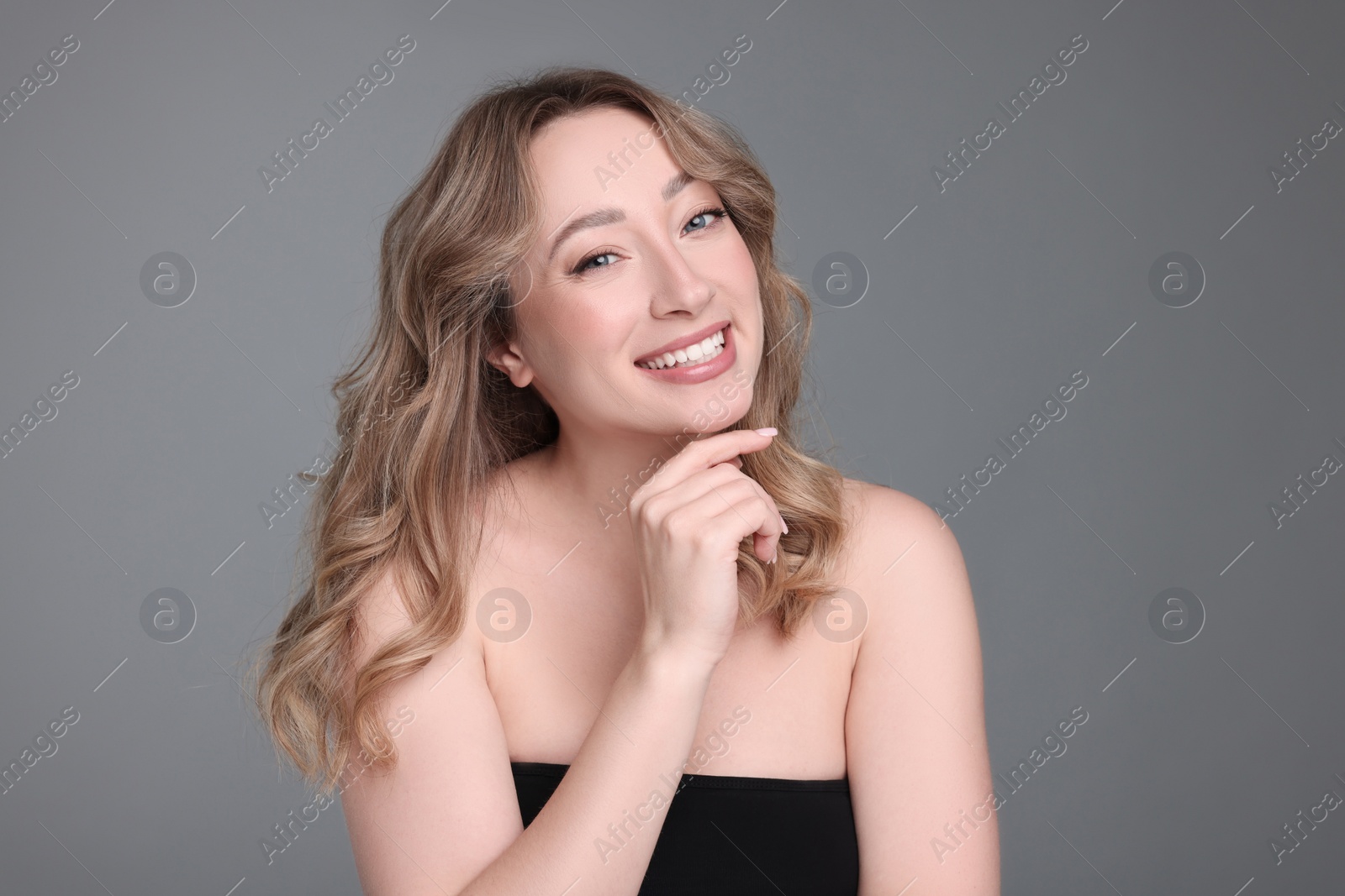 Photo of Portrait of smiling woman with curly hair on grey background