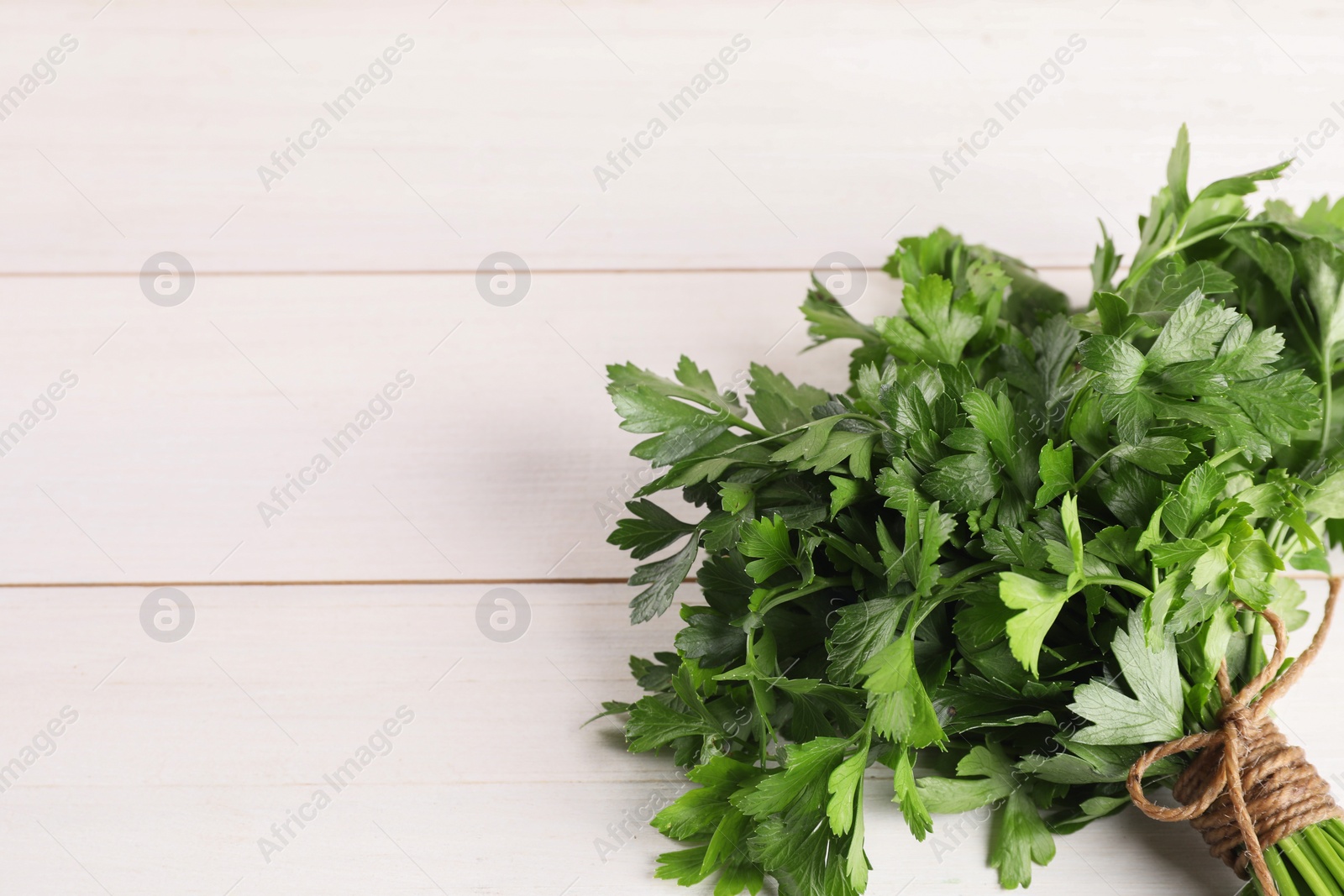 Photo of Bunch of fresh parsley on white wooden table, top view. Space for text