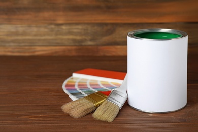 Can of paint, brushes and color palette samples on wooden table. Space for text