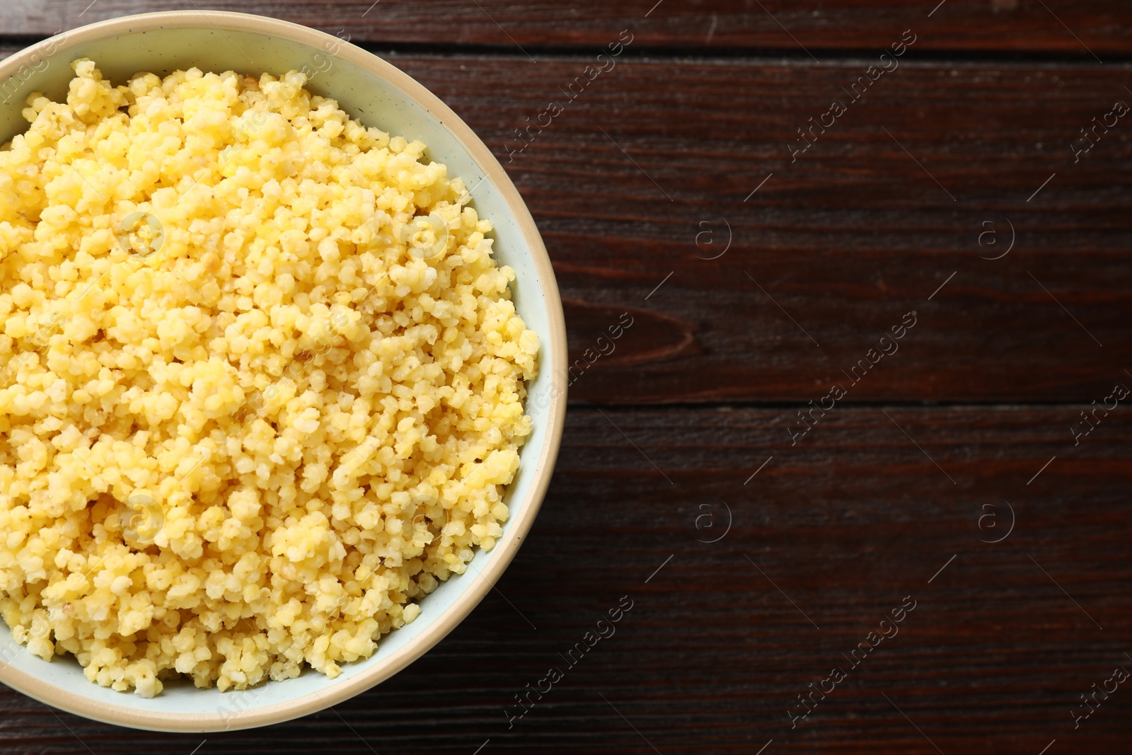 Photo of Tasty millet porridge in bowl on wooden table, top view. Space for text