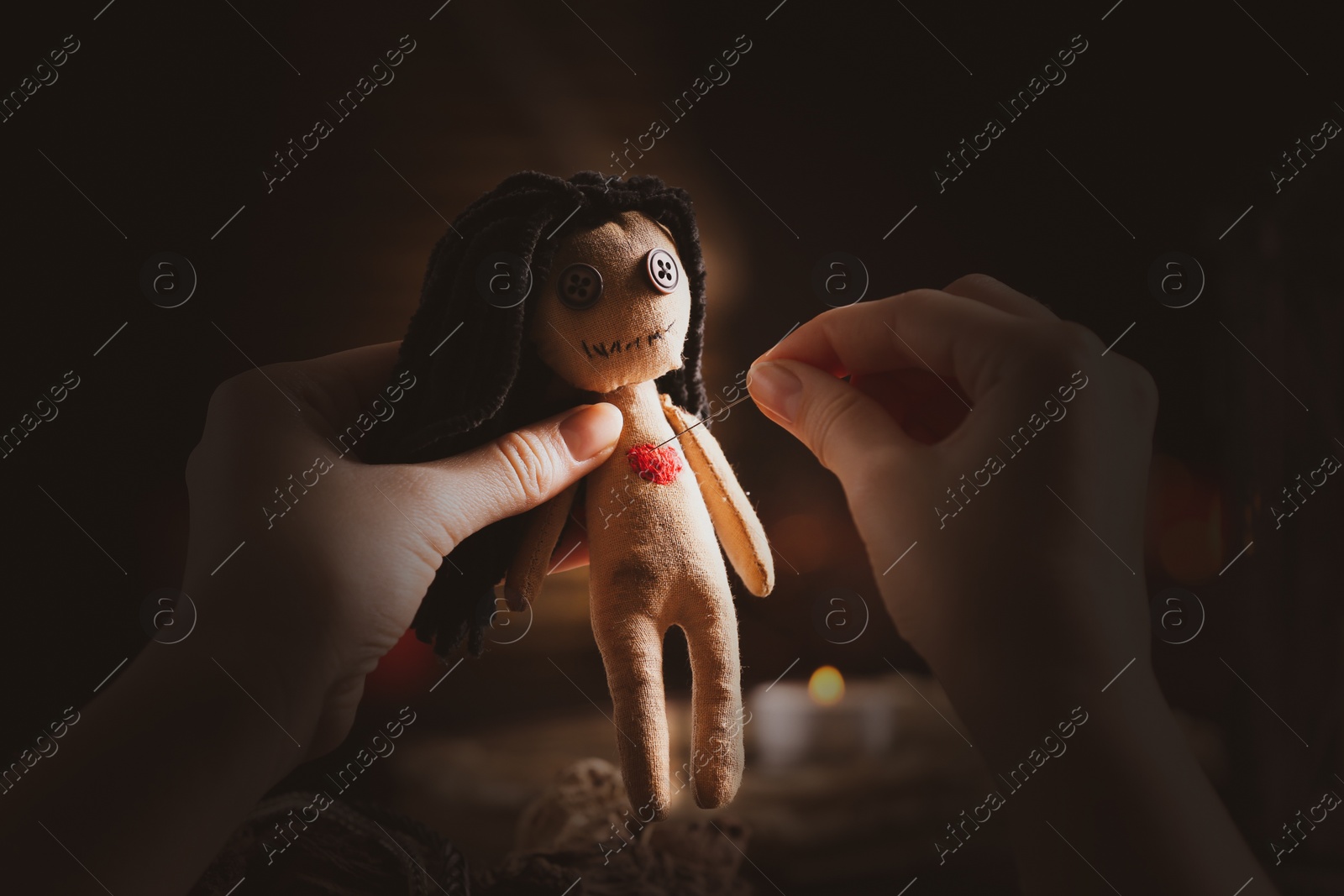 Image of Woman pricking female voodoo doll's heart with pin at table, closeup