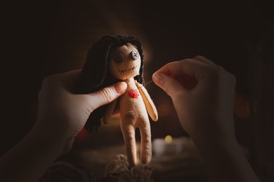 Image of Woman pricking female voodoo doll's heart with pin at table, closeup