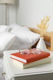 Books and glasses on white wooden bedside table in bedroom, space for text