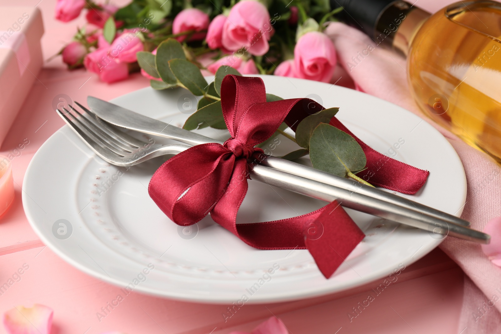 Photo of Romantic place setting. Plate, cutlery, eucalyptus branch and roses on pink table, closeup