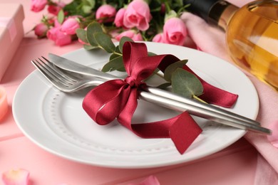 Photo of Romantic place setting. Plate, cutlery, eucalyptus branch and roses on pink table, closeup