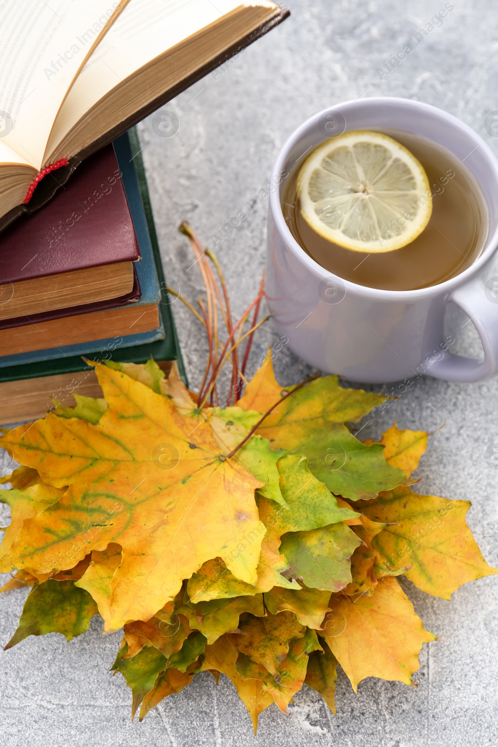 Photo of Yellow maple leaves, books and cup of tea on light gray table. Autumn atmosphere