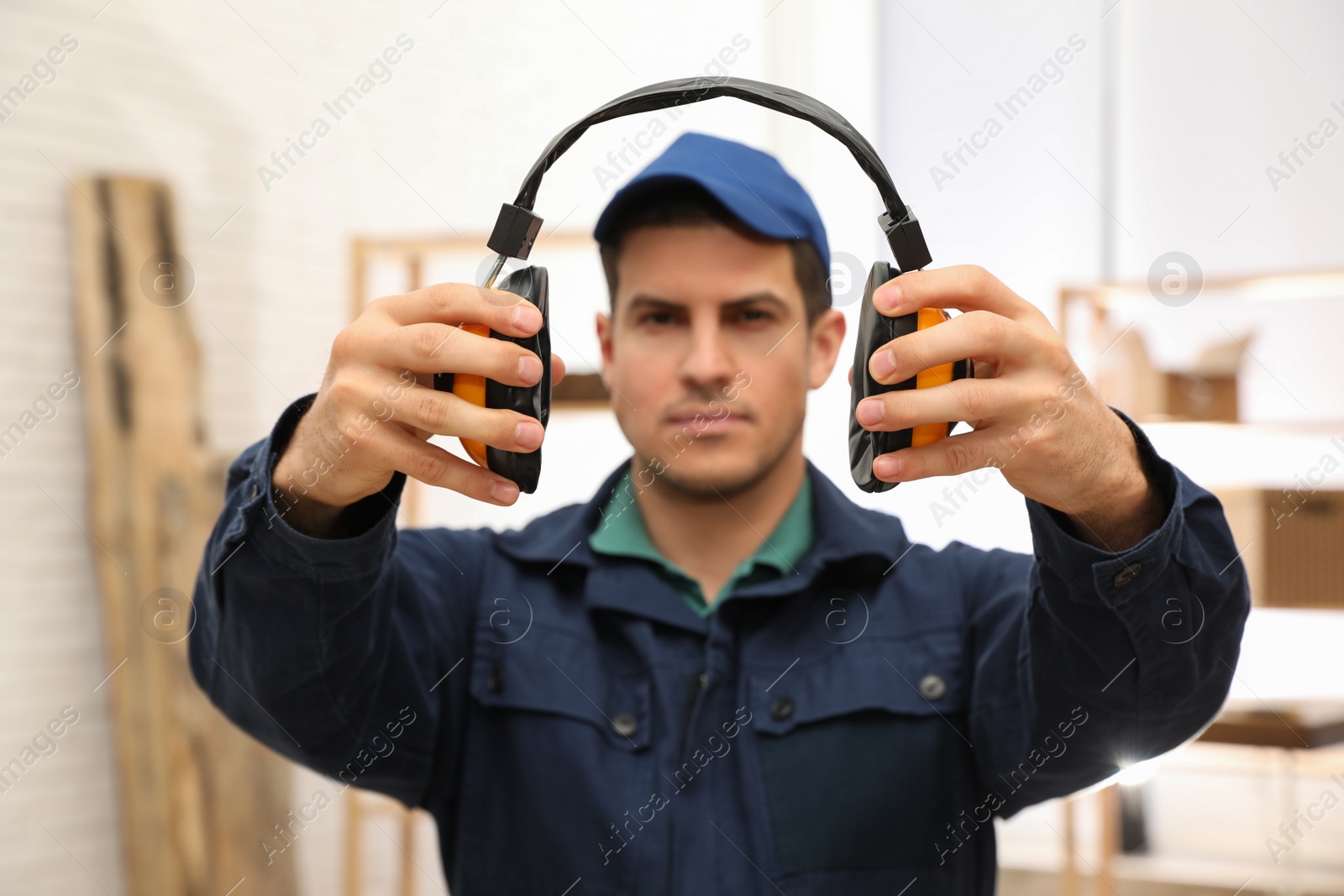 Photo of Worker holding safety headphones indoors, focus on hands. Hearing protection device