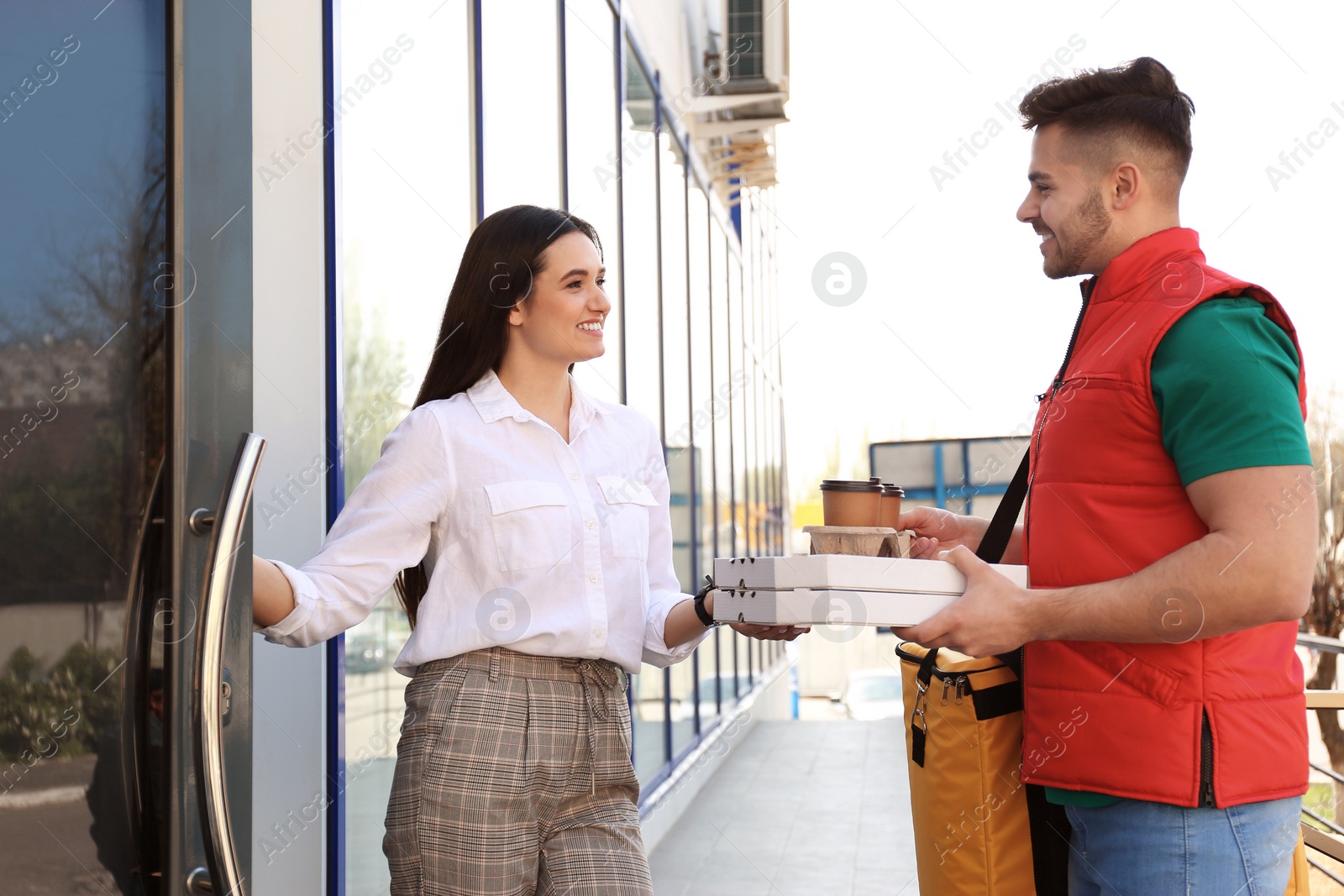Photo of Courier giving order to young woman at open door. Food delivery service