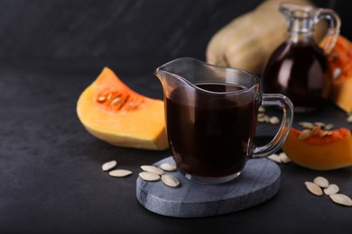 Photo of Fresh pumpkin seed oil in glass pitcher on dark grey table. Space for text