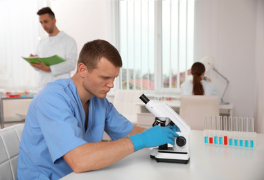 Photo of Scientist with microscope at table and colleagues in laboratory. Medical research