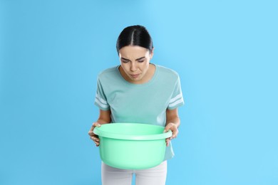 Photo of Woman with basin suffering from nausea on light blue background. Food poisoning