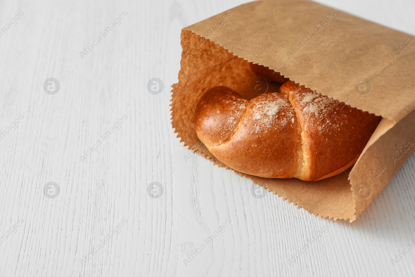 Photo of Paper bag with pastry on light wooden background. Space for text