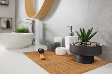 Photo of Potted artificial plant and toiletries near sink on bathroom vanity