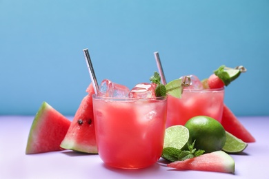 Photo of Tasty watermelon drink and fresh fruits on violet table against light blue background