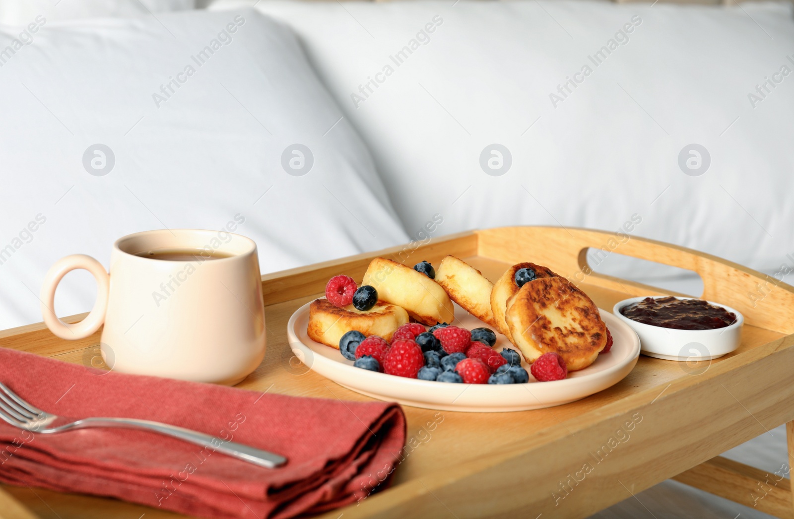 Photo of Tasty breakfast served in bedroom. Cottage cheese pancakes with fresh berries and coffee on wooden tray