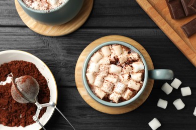 Photo of Cups of aromatic hot chocolate with marshmallows and cocoa powder on dark gray wooden table, flat lay