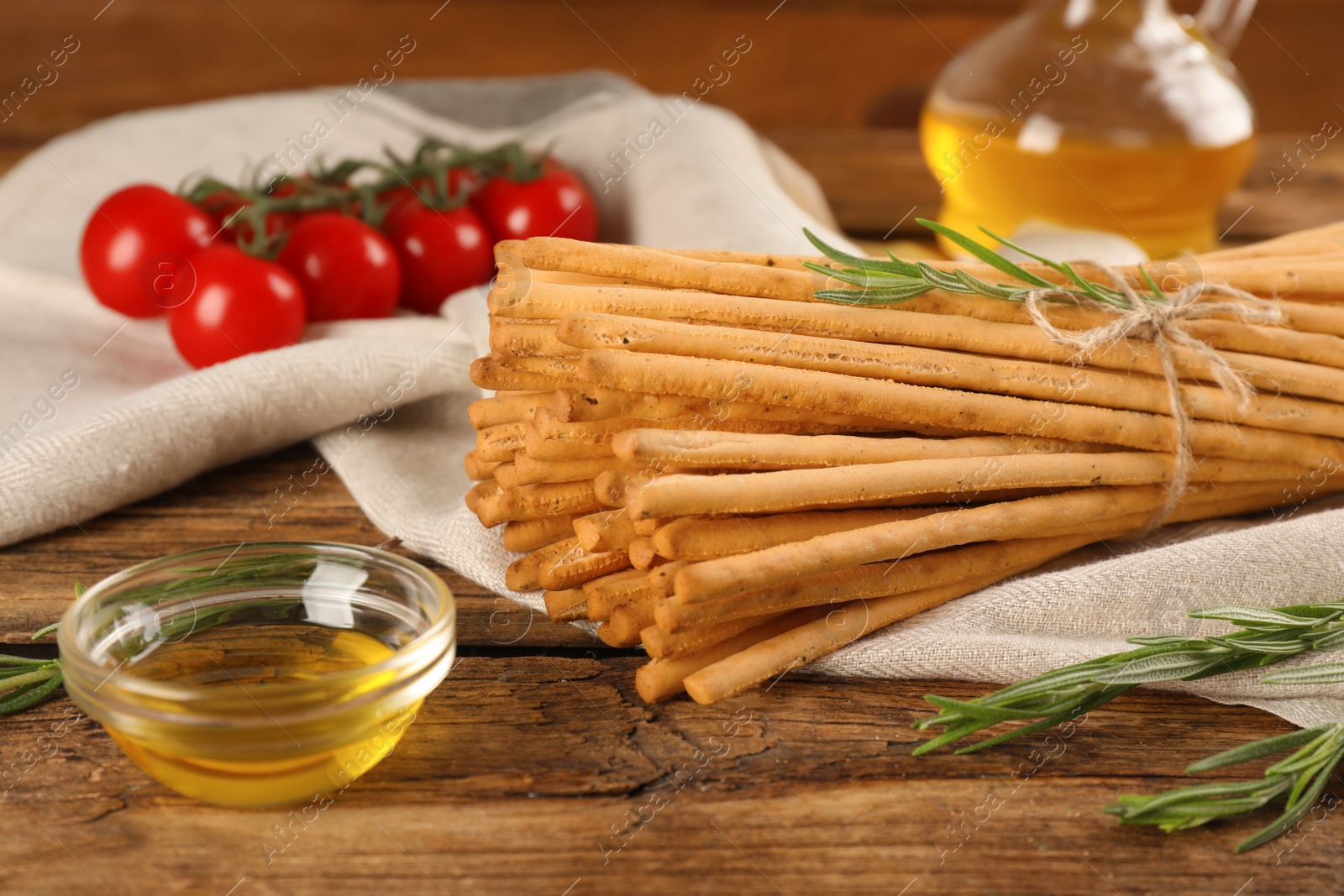 Photo of Delicious grissini sticks, oil, rosemary and tomatoes on wooden table