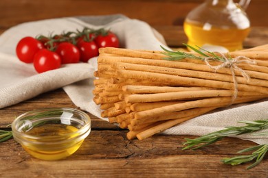 Delicious grissini sticks, oil, rosemary and tomatoes on wooden table
