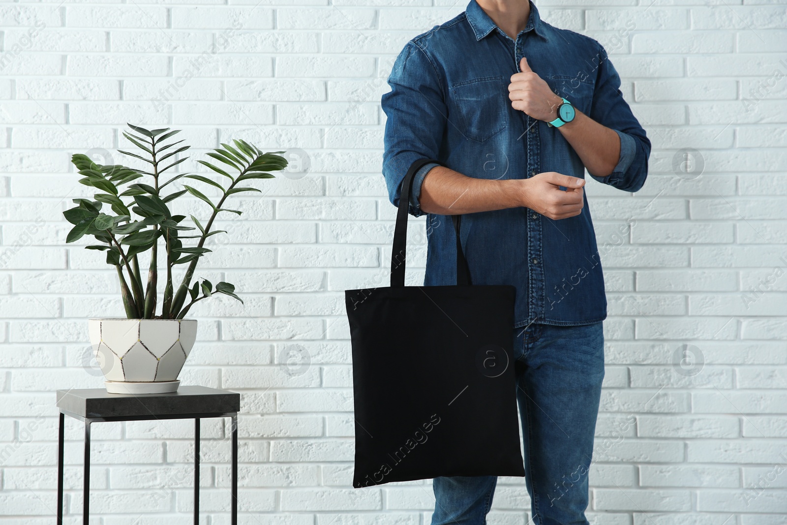 Photo of Young man holding textile bag against brick wall, closeup.  Mockup for design