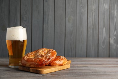 Tasty pretzels and glass of beer on wooden table, space for text