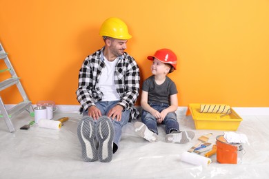 Father and son with repair tools near orange wall