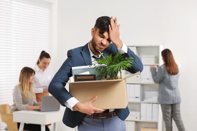 Photo of Unemployment problem. Frustrated man with box of personal belongings in office