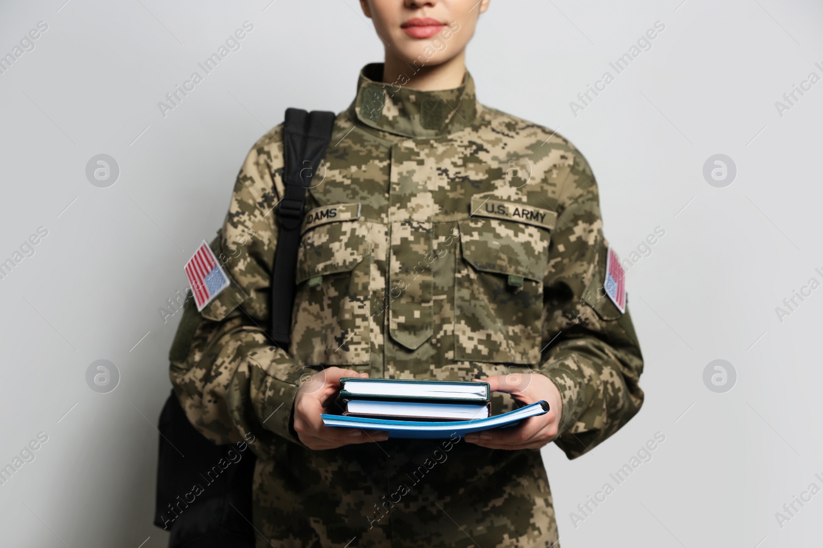 Photo of Female soldier with notebooks and backpack on light grey background, closeup. Military education