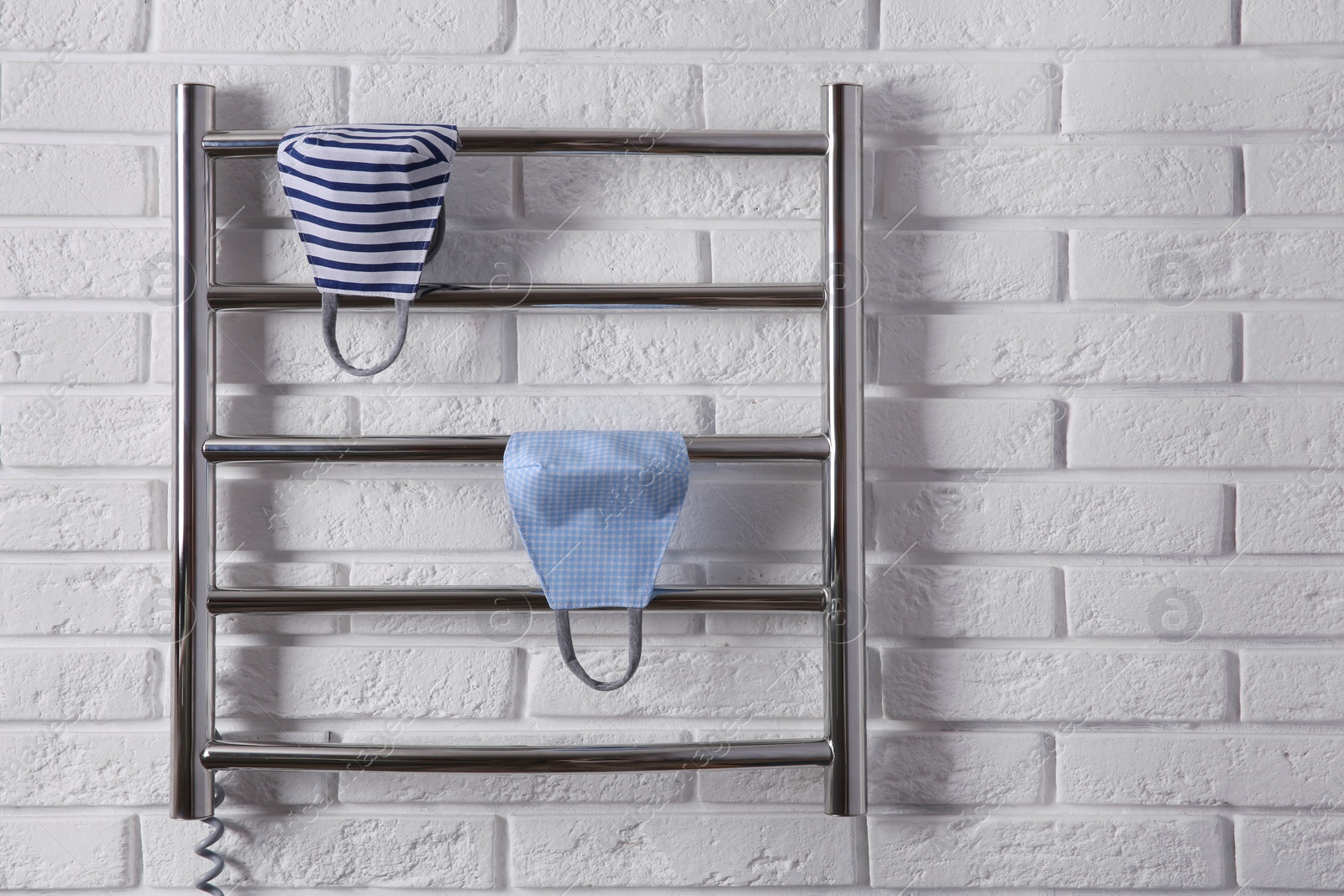 Photo of Modern heated towel rail with cloth face masks on white brick wall