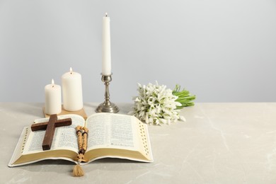 Church candles, wooden cross, rosary beads, Bible and flowers on light table. Space for text