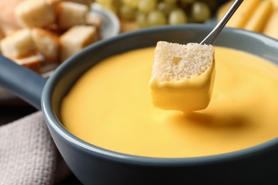 Photo of Dipping piece of bread into tasty cheese fondue, closeup