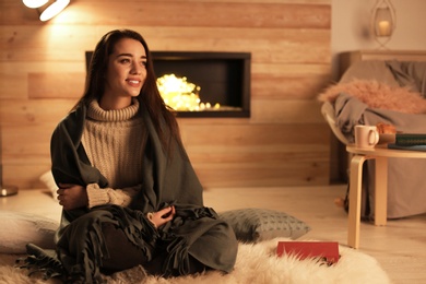 Photo of Young woman resting near decorative fireplace at home. Winter season