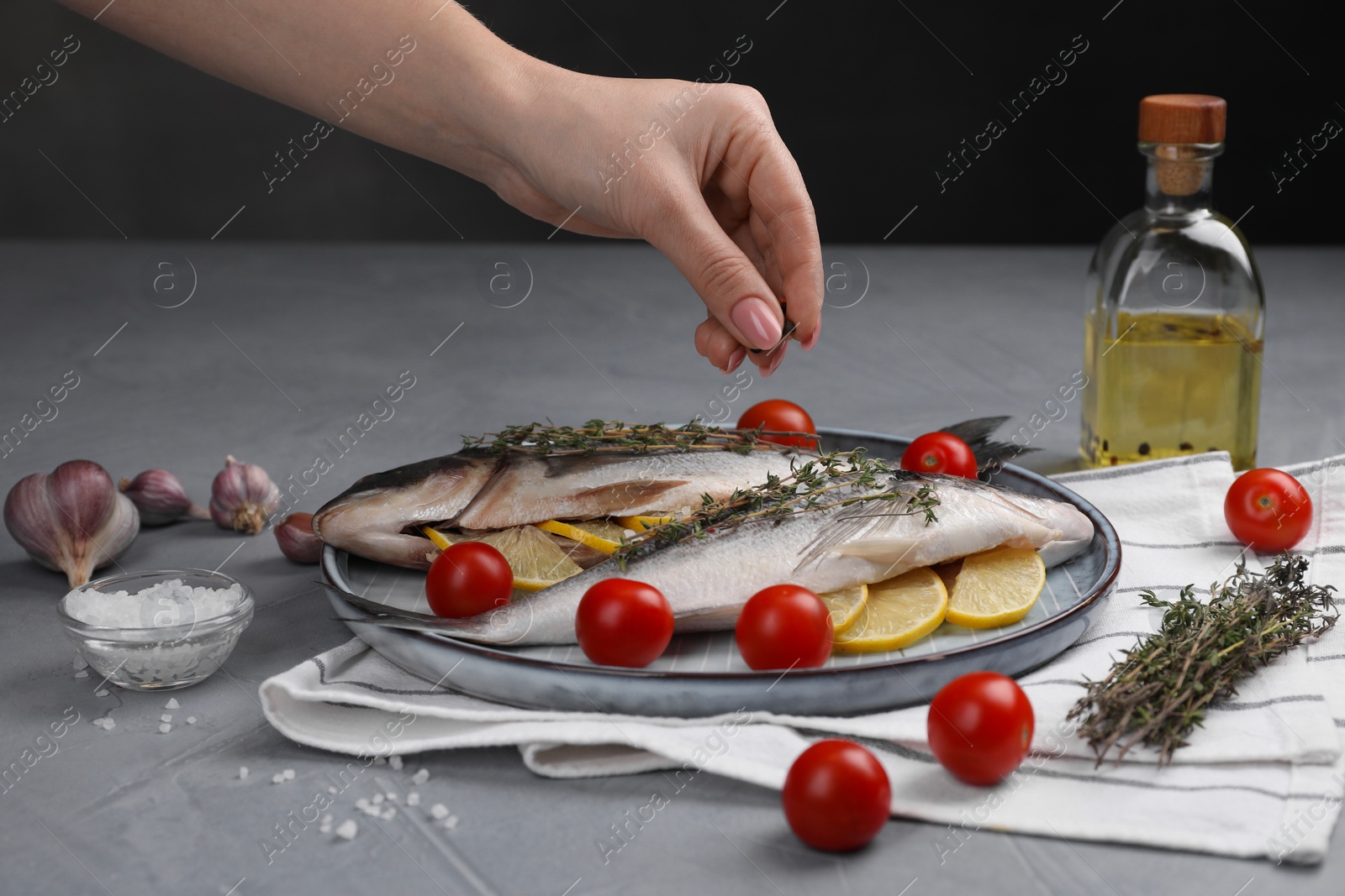 Photo of Woman adding spices onto raw dorado fish at grey table, closeup