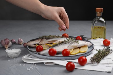 Woman adding spices onto raw dorado fish at grey table, closeup