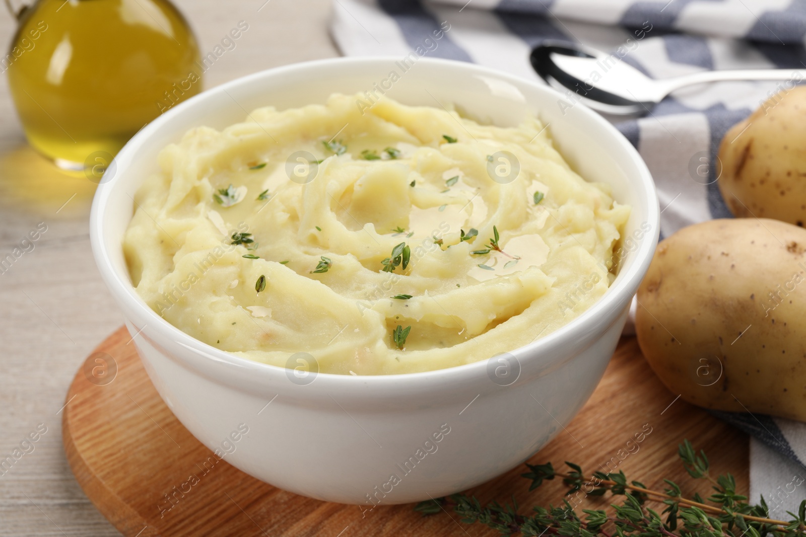 Photo of Bowl of tasty mashed potato with rosemary and olive oil on beige wooden table, closeup