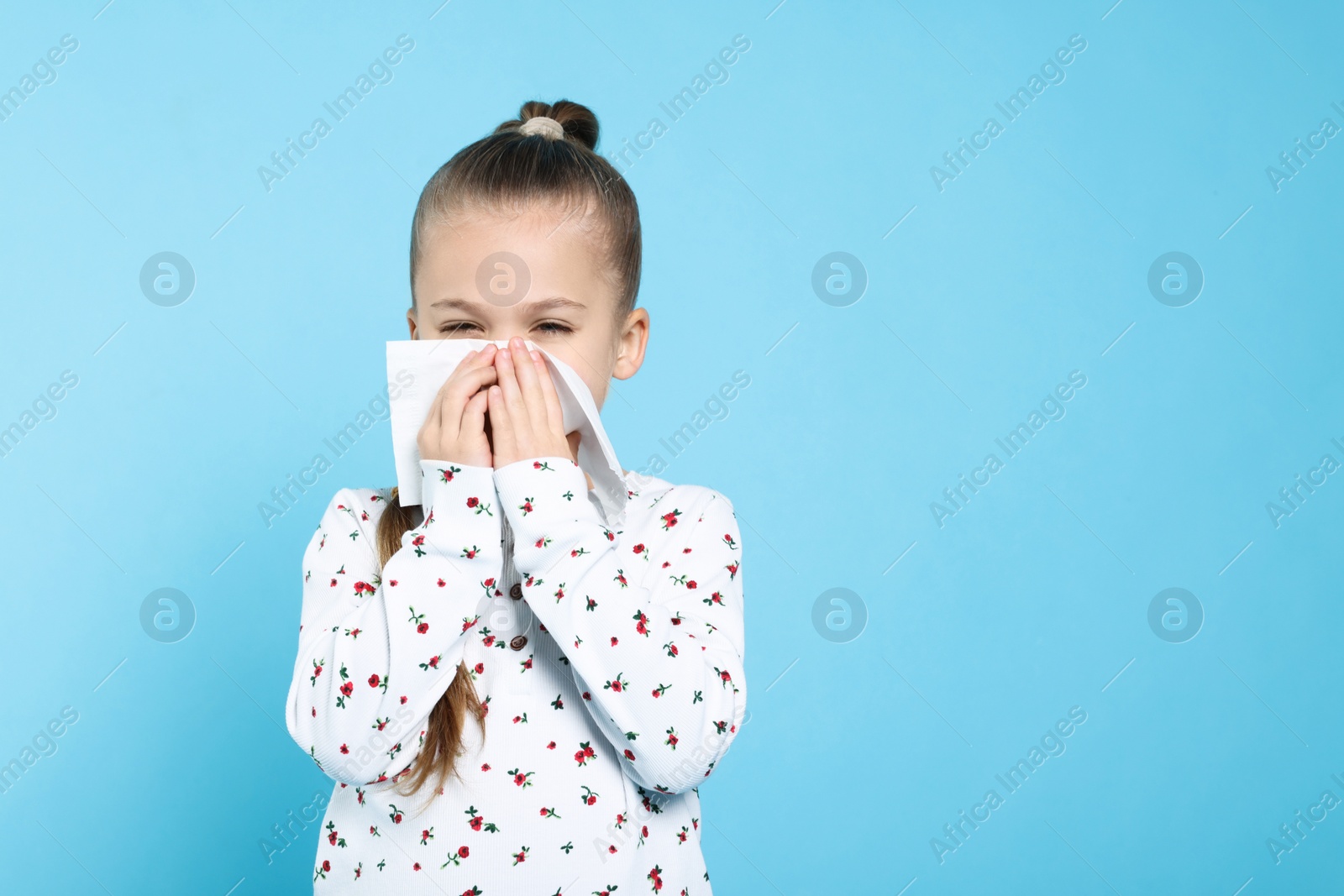 Photo of Sick girl blowing nose in tissue on turquoise background, space for text. Cold symptoms